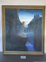 Framed painting showing a lady in a boat between cliffs with a castle in the background, overall view.