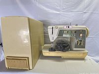 Image showing the Singer sewing machine and its hard cover case side by side on a white surface.