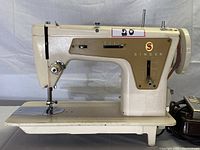 Front side view of the vintage Singer sewing machine showing the gold-tone panel, stitching controls, needle area, and logo.
