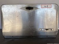 Closed view of the rectangular stainless steel bread storage unit showing scratches and worn areas on the surface, front handle and small label area.