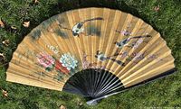 Full view of the large folding fan showing the floral and bird hand-painted design on a warm golden background, with wood and bamboo frame visible.
