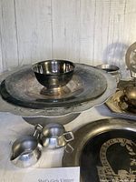 Detailed view of the silver 25th Anniversary plate with floral etching and other surrounding items including a silver bowl and aluminum serving plate.