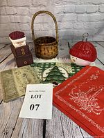 Lot arranged on wooden surface against a light brick wall background showing all items in the lot: Santa box decoration, wicker basket, snowman candy dish, book, and linen pieces.