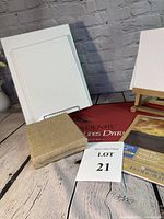 Photo showing multiple canvases including framed canvases (11x14 and 9x12), burlap covered canvases, canvas boards, small wooden easel, an 8x10 canvas pad and Strathmore large drawing pad, all arranged on a wooden surface against a brick wall background.