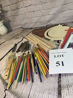 Photo showing assorted art brushes, colored pencils, charcoal, graphite pencils, wooden dowels, sketchpad, three art-related books and light wooden globe plaque.
