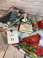 Photo shows all items in the lot including four large reusable Christmas-themed shopping bags, snowman figurine, book titled Christmas Treasury, two small candles, red ribbon clip, and decorative flag with cardinal and holly.