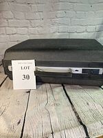 Black textured hard carrying case for electric typewriter with metal clasps and lock side mechanism.