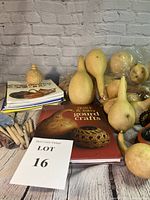 Photo showing assortment of dried gourds, chisel tools with wooden handles, several gourd craft books stacked, and a small card indicating Lot 16.
