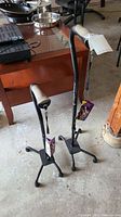 Photo showing two black adjustable canes standing upright with four-legged bases and beige padded handles, with original tags attached.