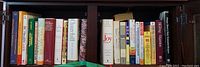 Books lined up on a wooden shelf showing various titles and sizes including religious and educational books.