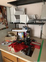Photo of workbench with several items including storage bins, gloves, small garden tools, propane torch, boxes of batteries and light bulbs.