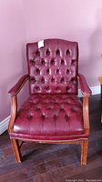 Front view of the Tudor upholstered chair showing burgundy tufted upholstery and brass studs.