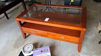 Top angle view showing wood frame, glass top inset, and two drawers with handles.