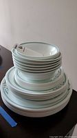 Stack of Corelle dinner plates, side plates and bowls with green stripe and floral decorative edge