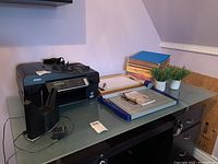 Black Epson all-in-one printer on desk with file folders, cutting board, and artificial plants