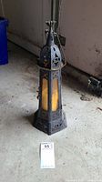 Full view of metal framed hexagonal lantern with candle, showing its tall height and detailed metal pattern with star cutouts.