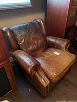 Front view of brown leather armchair showing worn seat cushion and studded armrests.