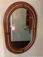 Full front view of the oval mirror mounted on a wall showing wood frame and rope detail.