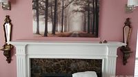 Two mirror sconces flanking a fireplace mantle with a wall painting above.