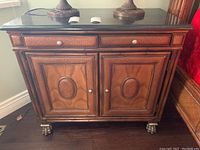 Front view of side table showing two drawers, two doors, wicker inlay and black top