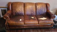 Front view of brown leather sofa bed showing three cushions, two cushions have damage with worn-through areas.