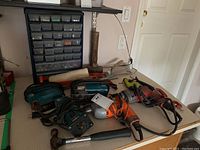 Photo of assorted power tools including drills, circular saw, and hammer on a table beneath the hardware organizer cabinet.