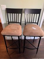 Two swivel stools with black metal frames and beige velvet seats against a wall with hardwood floor.