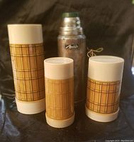 Silver Aladdin thermos and three plaid insulated covers with tops showing