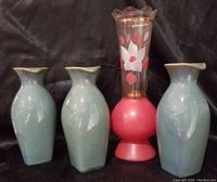 Photo of three ceramic light blue oil/vinegar bottles with pitcher-like spouts and a pink and clear glass Bartlett-Collins vase with flower decoration on black background.
