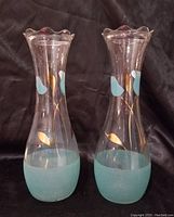 Photo showing two clear glass Bartlett-Collins vases with hand-painted teal and gold leaf designs, 9" tall, with frosted teal bases and scalloped rims.