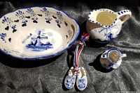 Four piece ceramic set with oval dish, pitcher, small vase, and miniature shoes displayed on black fabric