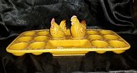 Front view of mustard yellow ceramic devilled egg plate with 13 egg-shaped wells and central tray featuring chick decoration, holding two hen-shaped salt and pepper shakers.