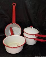 Three pieces of white enamelware with red trim including double boiler and two saucepans.