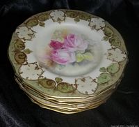 Stack of six decorative plates showing pink rose floral center with gold and green scrollwork border.