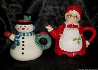 Front view of two holiday-themed ceramic teapots, a snowman and Mrs. Claus, showing details and colors.