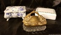 Three decorative trinket or dresser boxes photographed together on black background.