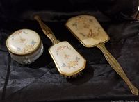 Front side of the dresser set showing the floral designs on the mirror, brush, and powder jar lid.