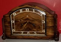 Front view of the "Foreign" mantel clock showing woodgrain dial with white numerals, gold-tone hands, curved wooden case, glass panel with metal trim.