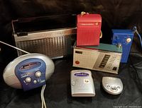 Top view showing all 7 vintage transistor radios in various shapes and colors on a dark surface