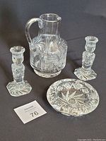 Photo of the crystal set including 2 candle holders, ashtray, and pitcher on a dark background.