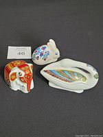 Three porcelain figurines: rabbit, elephant, and bird with colorful decorative patterns placed on dark background with lot number 46 card visible