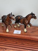 Pair of vintage hard plastic Clydesdale horse figurines side by side on wooden surface.