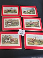 Six vintage cork-backed place mats featuring various hunting scenes with riders on horseback and dogs, each with a red and gold border, laid flat on a dark surface.