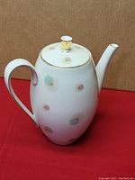 Full side view of white porcelain teapot with pastel colored starburst pattern and gold trim on handle, spout tip, and lid.