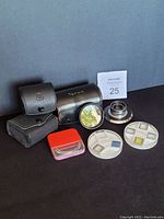 Front view of vintage camera items including Taron black leather case, other carrying cases, a collapsible lens, camera filters, and slide holders.