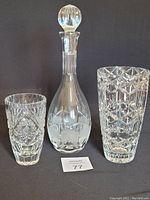 Photo showing vintage crystal decanter with a round stopper flanked by two crystal vases with different cut patterns, displayed against a black background.