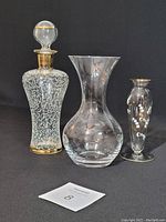 Full view of three items: glass decanter with gold trim and stopper, clear etched lead crystal vase, and small hand-painted glass vase