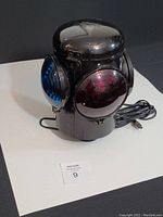 Front view showing black lamp with red and blue lenses, electrical cord coiled beside it.