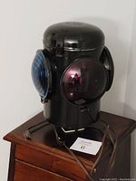 Full view of the lamp showing cylindrical black steel body with blue and red lenses, power cord, and plug.