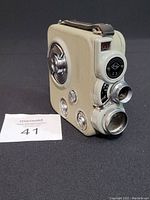 Front angled view of Eumig C3 vintage movie camera showing lens, viewfinder, and cream textured exterior with leather strap.